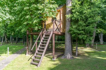 Charming wooden treehouse, located among tall trees in a serene park, on a sunny summer day.