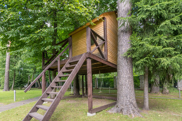 The wooden treehouse is located on an elevation among bright green trees in a quiet park, on a...