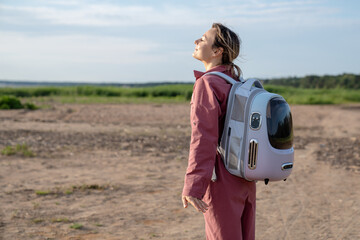 Happy carefree joyful woman basking in sun, looking up with closed eyes carrying cat backpack in...