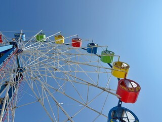 Looking up at a Ferris wheel with colorful cars against a clear azure sky. Concept of Festive ride adventure.