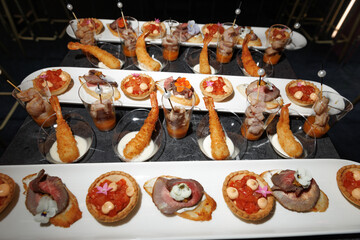 Elegant assortment of gourmet canapés, featuring shrimp, beef, and vegetable appetizers on white platters. Perfect for events, showcasing culinary artistry and inviting presentation.