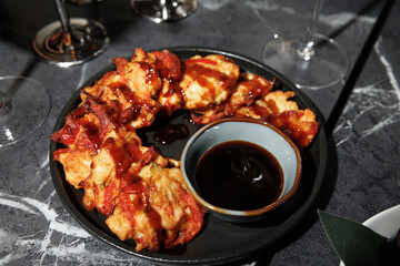 Plate of freshly cooked savory fritters drizzled with sauce, arranged around a bowl of dipping sauce. The setting is enhanced by elegant stemware on a dark marble surface.