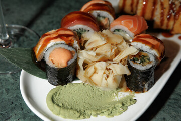 Delicious assortment of sushi rolls on a white plate with creamy wasabi and pickled ginger garnishes. Various sushi toppings and a leaf adorn the fresh presentation.
