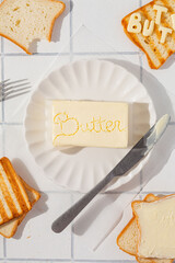 butter creative block with lettering "butter" on white plate and bread around.white background top view and copy space. stylish advertising or poster for butter brand 