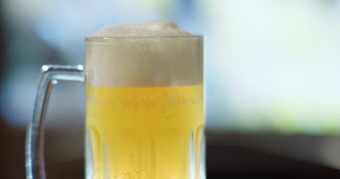 A glass mug of unfiltered beer on a blurry TV background