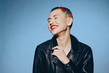 Smiling woman with colorful short hair and bright red lipstick wears black leather jacket against...