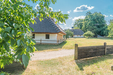 A thatched-roof house in a Central European village, situated on a grassy lawn with trees and a...