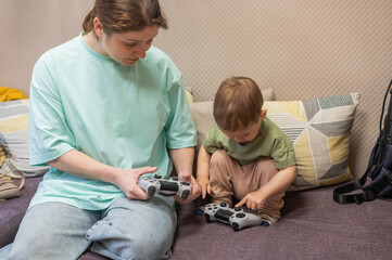 Caucasian woman teaches her little son to play console. Joystick in hands. 
