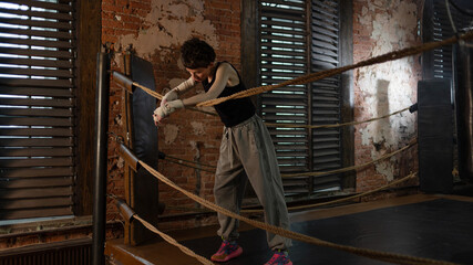 A woman with short hair in a boxing ring, pausing between intense workouts. stands leaning on the ropes, resting. Ready to fight, motivational cinematic look