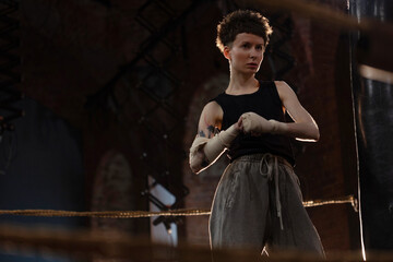 A woman in a boxing gym, portrait by the ropes, ready to fight, cinematic style photo, soft lighting, dark hall
