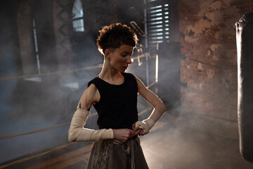 A woman in a boxing ring, wrapping an elastic bandage around her arms, preparing for boxing training. The photo is in a cinematic style, the light gives the mood to a sports motivational story about