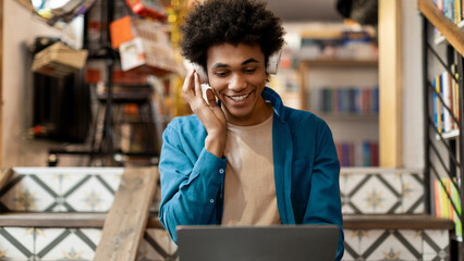 Happy African American guy using laptop during online class, touching headphones and smiling....