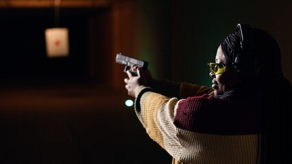 Portrait of joyous shooting range customer shooting targets with pistol, learning to operate...