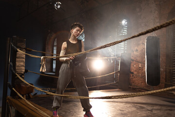 Boxer woman with short hair pausing on ropes, cinematic gym training atmosphere