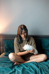 Teenage girl with cast on broken arm sitting on bed at home, recovering and using smartphone at...