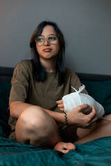 Teenage girl with cast on broken arm sitting on bed at home, recovering and using smartphone at...