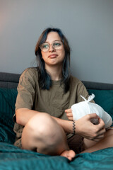 Teenage girl with cast on broken arm sitting on bed at home, recovering and using smartphone at...