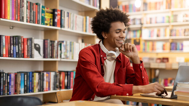 Positive African American student guy using laptop in college library, studying online or preparing for test, copy space. Technology-driven academic endeavors - Powered by Adobe