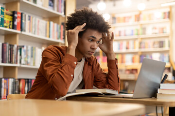 Lack of inspiration. Thoughtful black male student looking at laptop screen, sitting in college...
