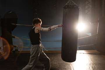 Cinematic boxing moment, female athlete training with punching bag in dramatic gym lights