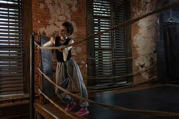 Short-haired boxer pausing workout, leaning on ring ropes with cinematic intensity