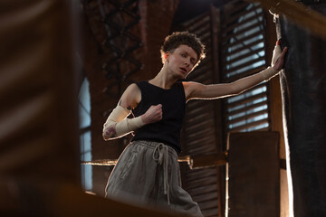 Short-haired boxer pausing workout, leaning on ring ropes with cinematic intensity