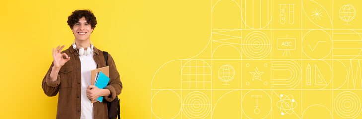 A student stands against a bright yellow wall, smiling and showing an OK gesture. He holds a stack of books and headphones, showcasing a positive attitude towards education and learning. © Prostock-studio