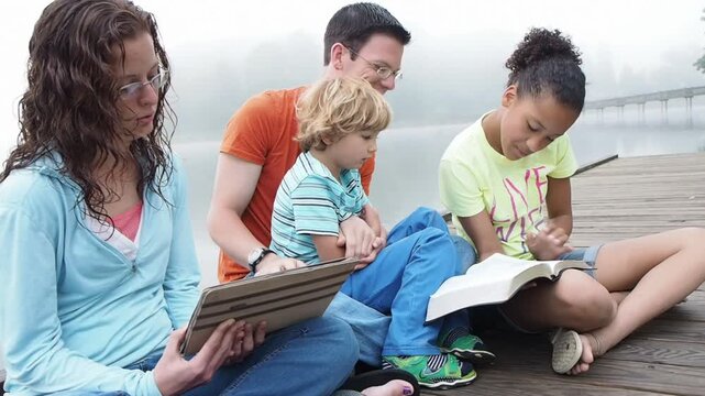 Panning Shots of Multicultural Family Doing Bible Study by Lake at Sunrise