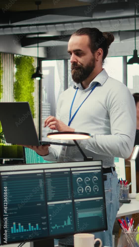 Poster vertical video male team leader monitoring analytics on a laptop in co working space, handling daily