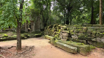 Ta Prohm, Cambodia - 3 July 2025. Stacked moss-covered stones and temple gateway stand in jungle...