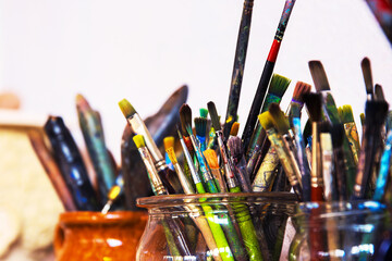 A collection of used paintbrushes varied with colorful stains  in glass and ceramic jars, arranged...