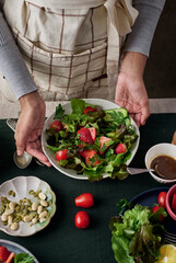 Unrecognizable female chef holding a plate of delicious summer salad with strawberry and lots of greens.