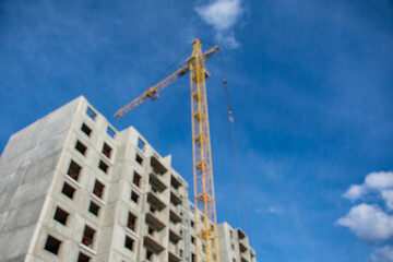 Blurred image captures the essence of a construction site, featuring multiple buildings and a towering crane under a vast sky.