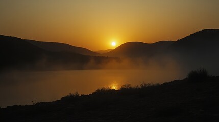 Sunrise over a misty lake, silhouetted hills