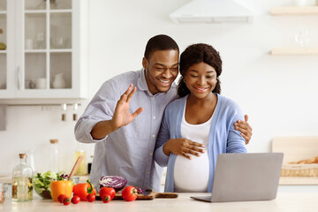 Cheerful pregnant black couple handsome man and woman with big belly having video call with their...