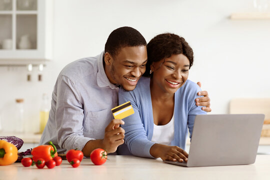 Joyful black couple using laptop and credit card in kitchen, shopping online while cooking. Excited african american family buying grocery on Internet during COVID-19 pandemic, copy space
