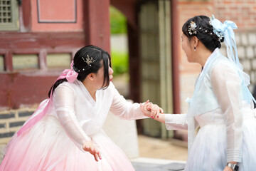 Two Korean women in their twenties hold hands beside a majestic historic structure at Gyeongbokgung...