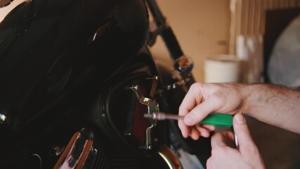 Hands work diligently on a motorcycle engine, using a green-handled screwdriver to fix components in a garage filled with tools and parts. - Powered by Adobe