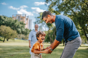 Father and son laughing together outdoors with grandfather nearby
