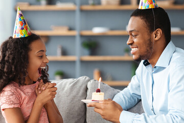 Loving black dad making birthday surprise for his emotional cute daughter, home interior. Excited...