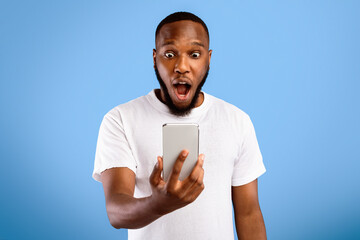 Wow News. Shocked Black Guy Holding Phone Reading Surprising Message Standing Posing With Opened...