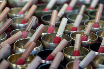 A bell vendor presents an array of handcrafted singing bowls in a vibrant market. Each bowl is accompanied by a wooden mallet, creating a colorful display of traditional music instruments.