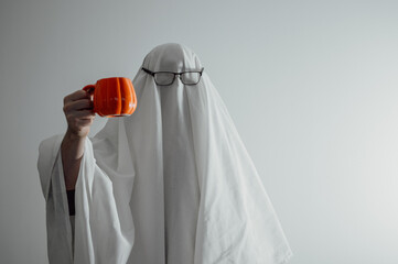 Person in costume of ghost hold pumpkin shaped cup.Halloween celebration banner with copy space