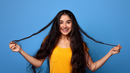 Hair Care And Therapy Treatment Concept. Portrait of smiling indian woman posing and holding dark...