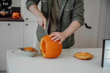 cropped image of Man in in the kitchen carving halloween lantern from pumpkin. October 31 celebration