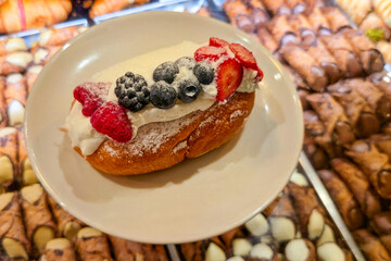 Traditional Italian maritozzo filled with whipped cream and topped with fresh berries, served on a...