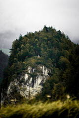 Kapelle auf bewaldetem Felsen in nebliger Berglandschaft