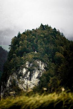 Kapelle auf bewaldetem Felsen in nebliger Berglandschaft