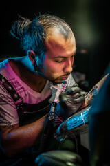 Man tattoo master with dreadlocks showing process creation tattoo, female body 