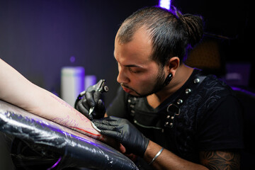 Man tattoo master with dreadlocks showing process creation tattoo, female body 